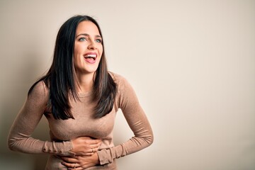 Obraz premium Young brunette woman with blue eyes wearing casual sweater over isolated white background smiling and laughing hard out loud because funny crazy joke with hands on body.