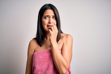 Young brunette woman with blue eyes wearing shower towel after bath over white background looking stressed and nervous with hands on mouth biting nails. Anxiety problem.