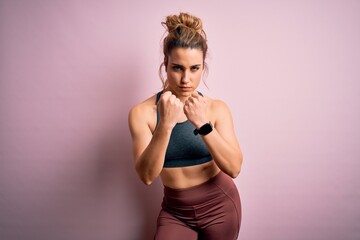 Obraz premium Young beautiful blonde sportswoman doing sport wearing sportswear over pink background Ready to fight with fist defense gesture, angry and upset face, afraid of problem