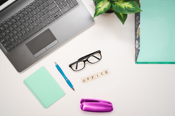 White desk with laptop, printer, supplies and "office" letters on wooden blocks.Top view