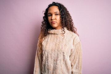 Young beautiful woman with curly hair wearing casual sweater standing over pink background Relaxed with serious expression on face. Simple and natural looking at the camera.