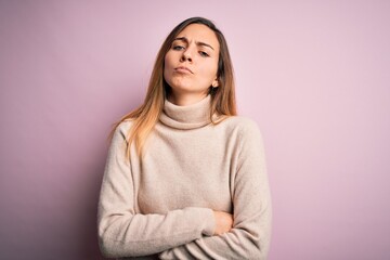 Beautiful blonde woman with blue eyes wearing turtleneck sweater over pink background skeptic and...