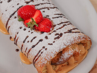 Sponge cake with tea on a wooden table.
One biscuit roll in a white plate lies on a wooden table  close-up.