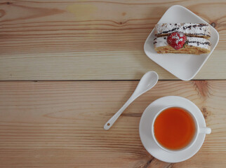 Sponge cake with tea on a wooden table.
One slice of biscuit roll and a mug of black tea on a wooden table, close-up and with place for text on the right.