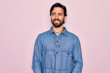 Young handsome hispanic bohemian man wearing hippie style over pink background looking away to side with smile on face, natural expression. Laughing confident.