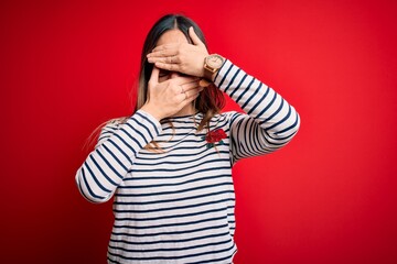 Young beautiful blonde woman with blue eyes wearing glasses standing over red background Covering eyes and mouth with hands, surprised and shocked. Hiding emotion