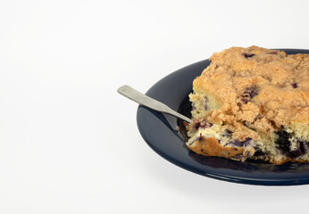Classic blueberry buckle as grandma made with a silver fork on a dark blue plate against a white background.