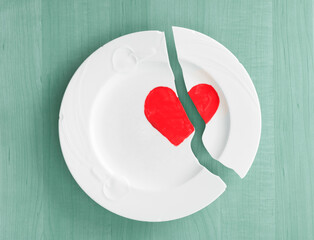 Broken Heart Concept representing divorce with broken white plate on teal wood board background with copy space.