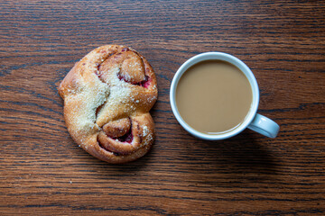 A cup of coffee with fresh bun. Bakery on wooden background. Top view