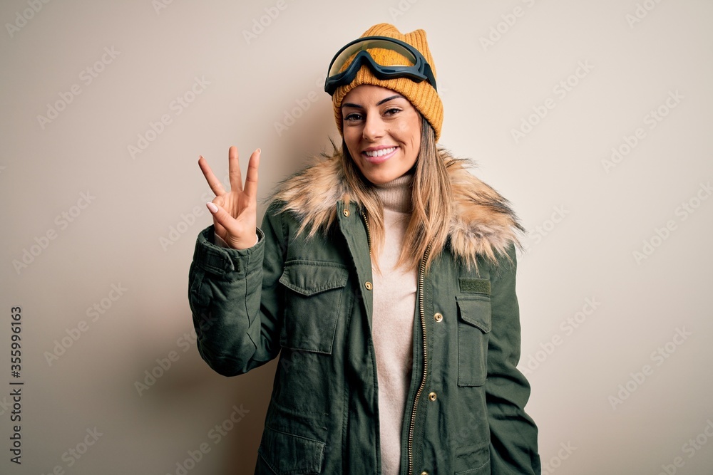 Sticker young brunette skier woman wearing snow clothes and ski goggles over white background showing and po