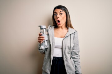 Young beautiful brunette sporty woman drinking bottle of water over isolated white background scared in shock with a surprise face, afraid and excited with fear expression
