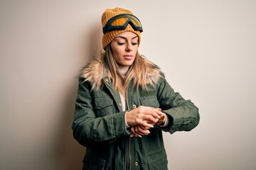 Young brunette skier woman wearing snow clothes and ski goggles over white background Checking the time on wrist watch, relaxed and confident