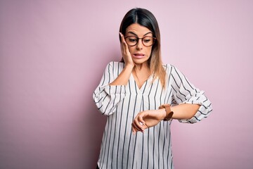 Young beautiful woman wearing casual striped t-shirt and glasses over pink background Looking at...