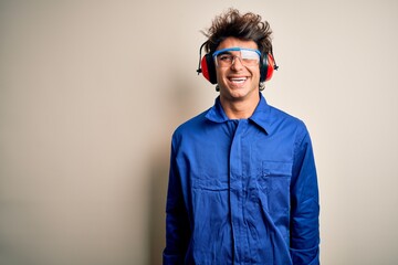 Young constructor man wearing uniform and earmuffs over isolated white background with a happy and cool smile on face. Lucky person.