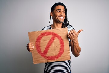 Young handsome african american man with dreadlocks holding banner with prohibited signal pointing...
