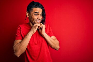 Young handsome african american afro man with dreadlocks wearing red casual t-shirt laughing nervous and excited with hands on chin looking to the side