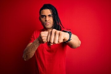 Young handsome african american afro man with dreadlocks wearing red casual t-shirt Punching fist to fight, aggressive and angry attack, threat and violence