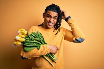 Young african american afro romantic man with dreadlocks holding bouquet of yellow tulips confuse...