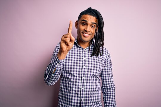 Young handsome african american afro man with dreadlocks wearing casual shirt pointing finger up with successful idea. Exited and happy. Number one.