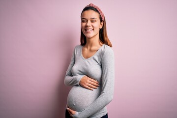 Young beautiful teenager girl pregnant expecting baby over isolated pink background happy face...