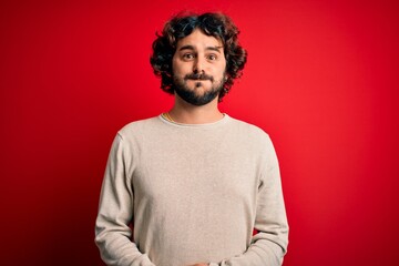 Fototapeta na wymiar Young handsome man with beard wearing casual sweater standing over red background puffing cheeks with funny face. Mouth inflated with air, crazy expression.