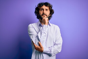 Young handsome business man with beard wearing shirt standing over purple background with hand on chin thinking about question, pensive expression. Smiling and thoughtful face. Doubt concept.