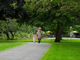 Mother and daughter walk the paved walkway in the springtime garden among the lawns and trees