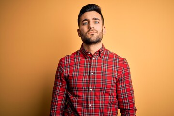 Fototapeta premium Young handsome man wearing casual shirt standing over isolated yellow background Relaxed with serious expression on face. Simple and natural looking at the camera.