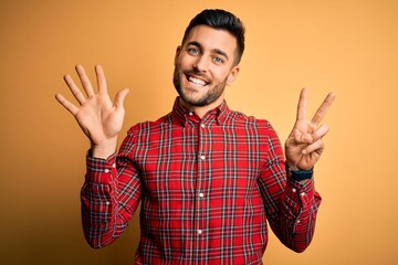 Naklejka premium Young handsome man wearing casual shirt standing over isolated yellow background showing and pointing up with fingers number seven while smiling confident and happy.