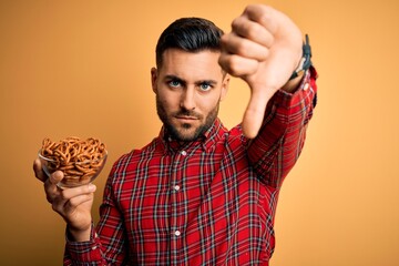 Young handsome man holding bowl with potato chips over isolated yellow background with a happy face standing and smiling with a confident smile showing teeth