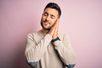 Young handsome man wearing casual sweater standing over isolated pink background sleeping tired dreaming and posing with hands together while smiling with closed eyes.