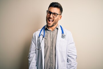 Young doctor man wearing glasses, medical white robe and stethoscope over isolated background...