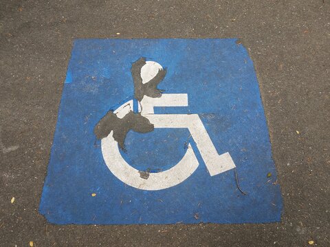 weathered blue wheelchair symbol on black asphalt