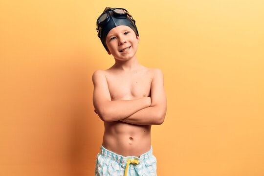 Cute blond kid wearing swimwear and swimmer glasses happy face smiling with crossed arms looking at the camera. positive person.