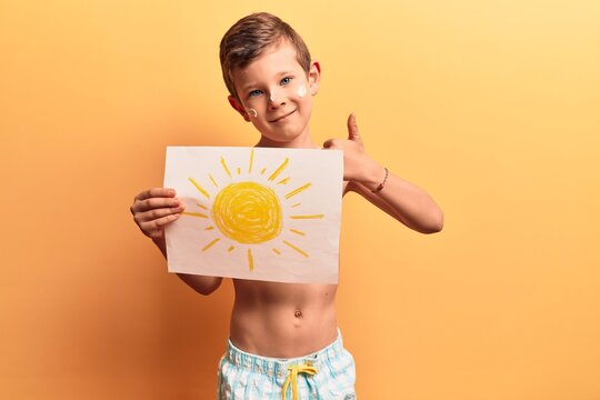 Cute blond kid wearing swimwear and summer hat smiling happy and positive, thumb up doing excellent and approval sign