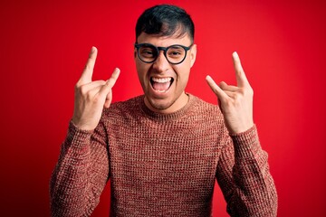 Young handsome hispanic man wearing nerd glasses over red background shouting with crazy expression...