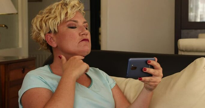 Portrait of a stressed middle aged woman looking into mirror feeling sad about fat neck