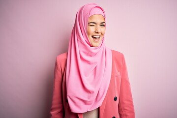 Fototapeta premium Young beautiful girl wearing muslim hijab standing over isolated pink background winking looking at the camera with sexy expression, cheerful and happy face.
