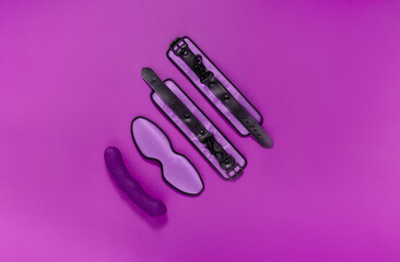 Sex toys handcuffs, sleeping mask and vibrator on bright purple background. Sex and pleasure concept.