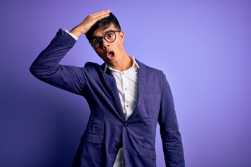 Young handsome business man wearing jacket and glasses over isolated purple background surprised...