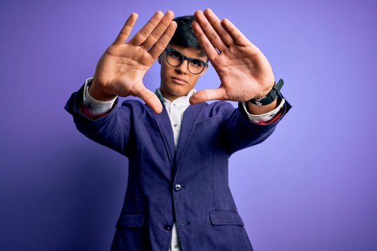 Young handsome business man wearing jacket and glasses over isolated purple background doing frame using hands palms and fingers, camera perspective