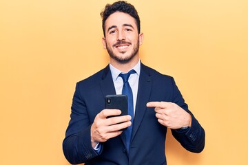 Young hispanic man wearing suit using smartphone smiling happy pointing with hand and finger