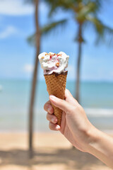 Female hand holding ice cream in waffle cone against summer beach background