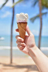 Ice cream cone held up to sky on summer beach background.