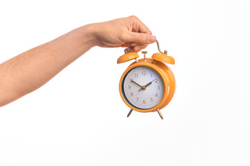 Hand of caucasian young man holding yellow vintage alarm clock over isolated white background