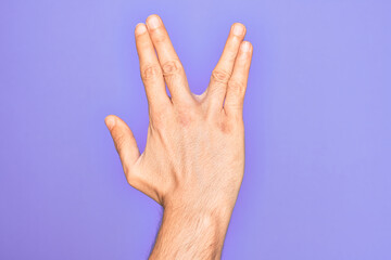 Hand of caucasian young man showing fingers over isolated purple background greeting doing Vulcan salute, showing back of the hand and fingers, freak culture