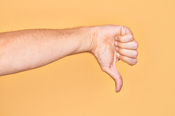 Hand of caucasian young man showing fingers over isolated yellow background doing thumbs down...