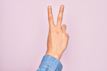 Hand of caucasian young man showing fingers over isolated pink background counting number 2 showing two fingers, gesturing victory and winner symbol