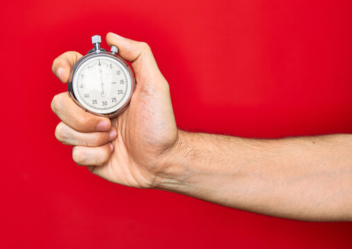 Beautiful hand of man holding stopwatch doing countdown over isolated red background