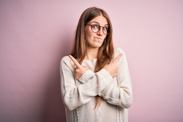 Fototapeta premium Young beautiful redhead woman wearing casual sweater and glasses over pink background Pointing to both sides with fingers, different direction disagree